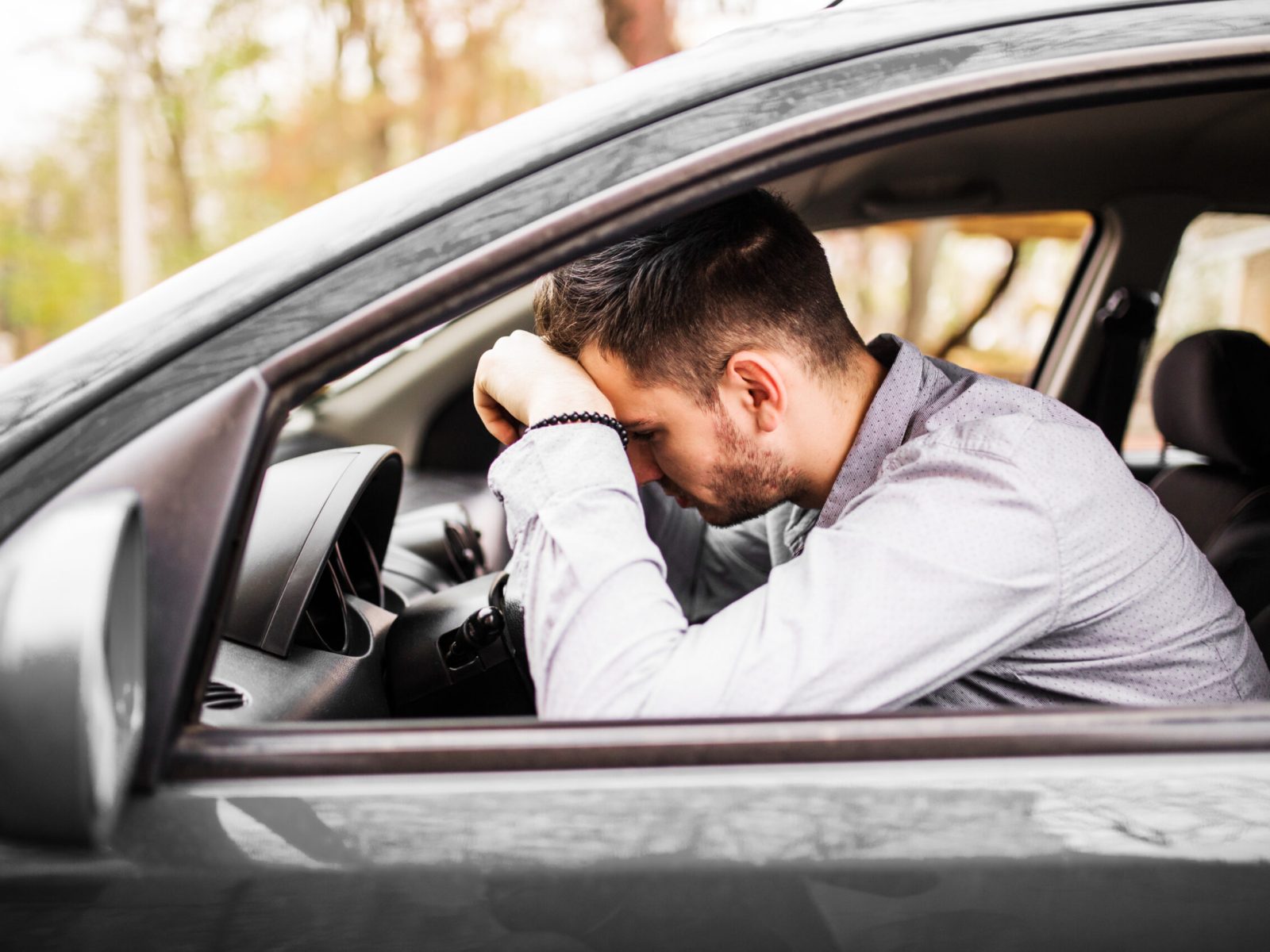 Young man sitting in his car very upset and stressed after hard failure and moving in traffic jam